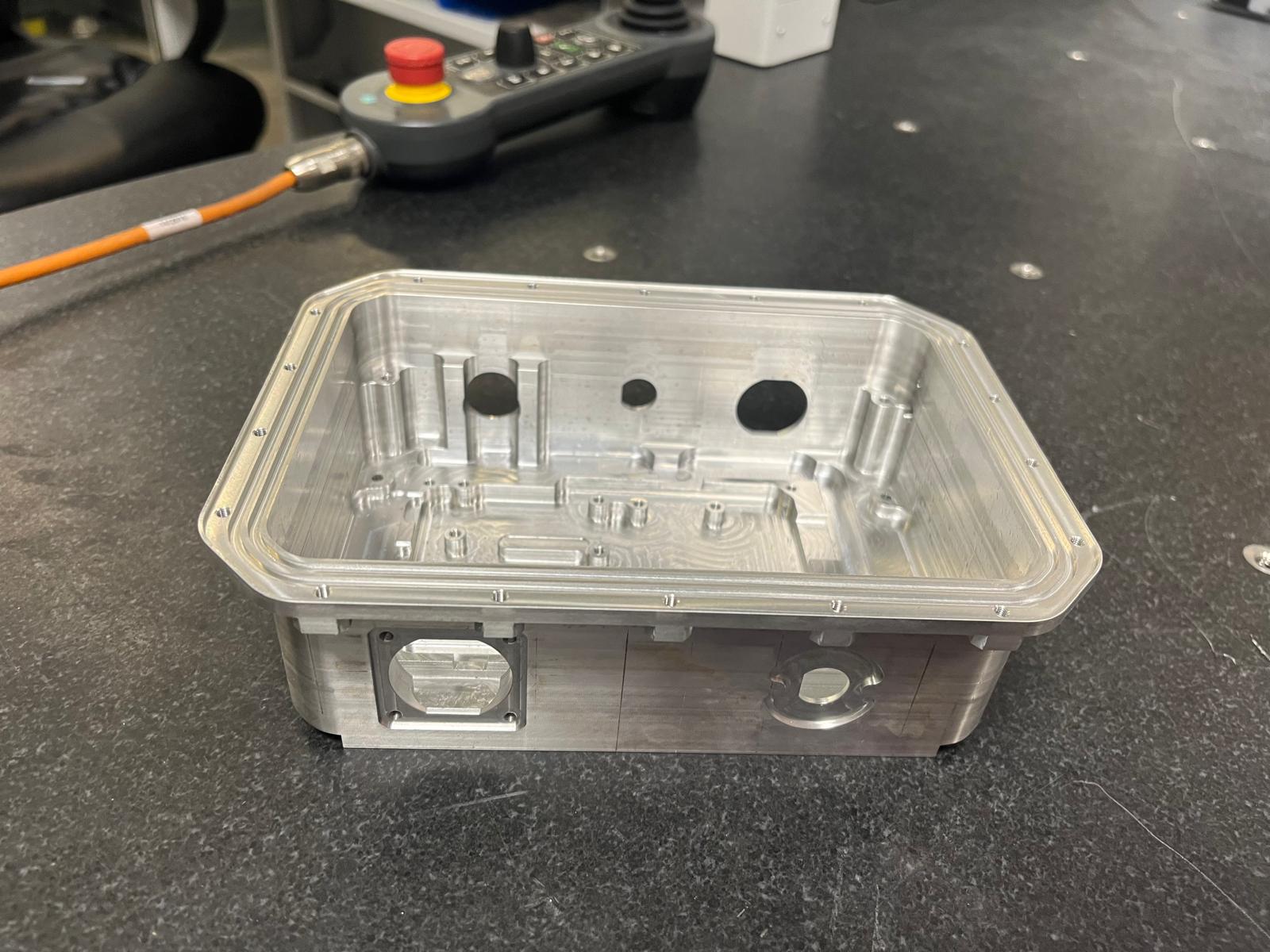 The machined aluminium box includes internal pockets, raised bosses, fixing points and a continuous lid interface.